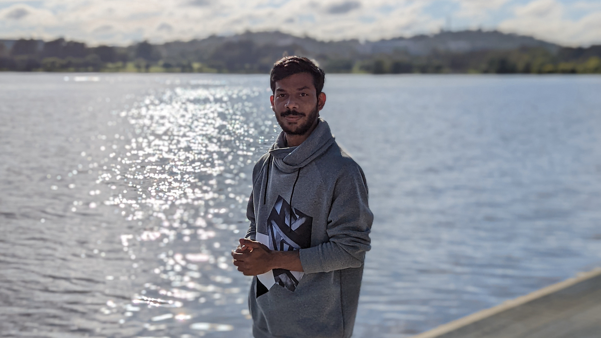 Nakul stands by Lake Burley Griffin and faces the camera.