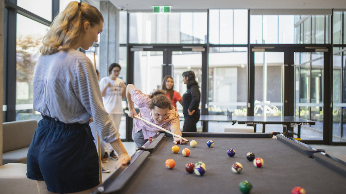Two students play pool in a student residence.