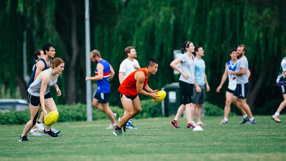 A mixed team practice footy on a grassy ANU oval.