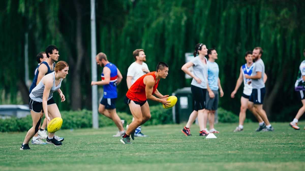 A mixed team of ANU students play footy on the oval. 