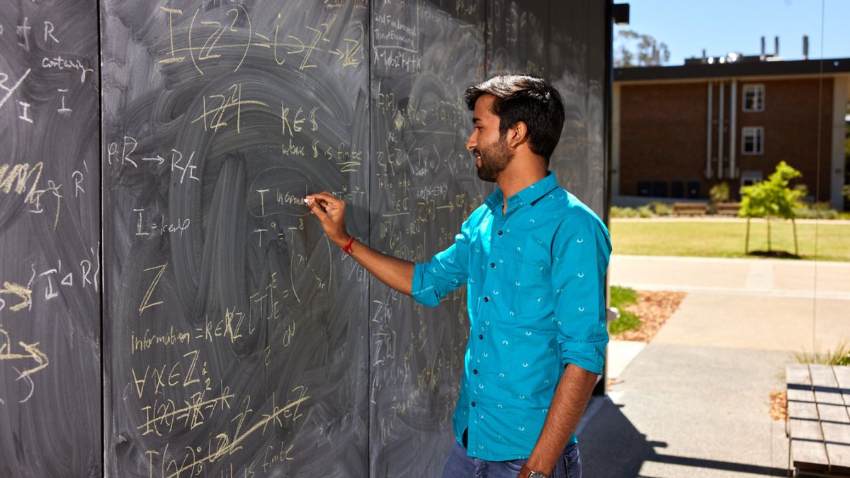 An ANU student writing on an outdoor blackboard.
