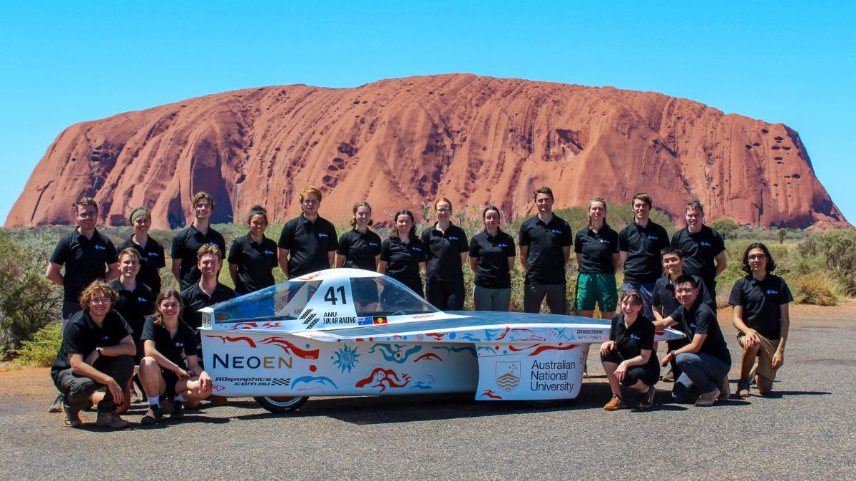 The ANU Solar Racing team stand in front of Uluru in the Northern Territory with their built solar car.