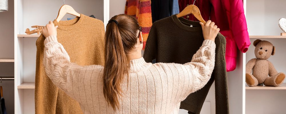 A woman looking into her wardrobe, holding up two jumpers on hangers