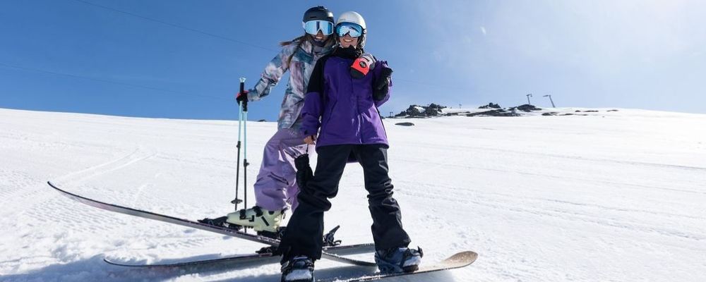 Two women in the snow at Perisher, one on skis, and one on a snowboard – both smiling at the
            camera.