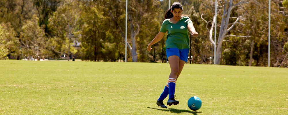 Female football player kicking ball on oval