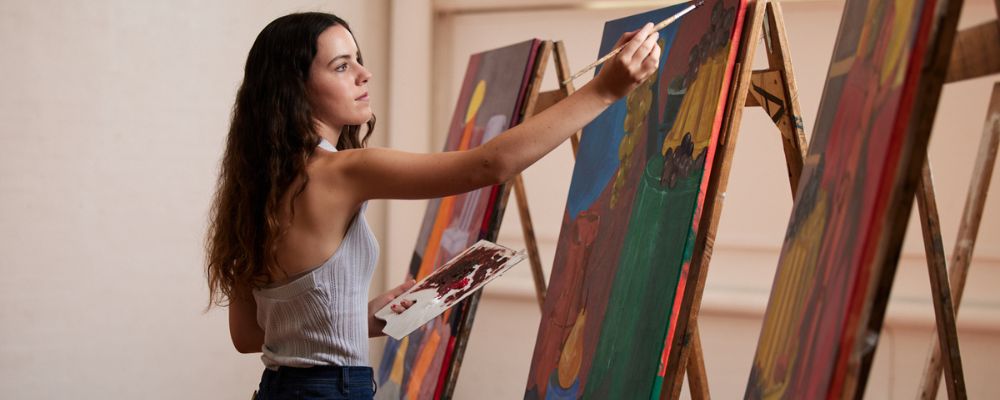 Female art student painting on canvas holding an easel
