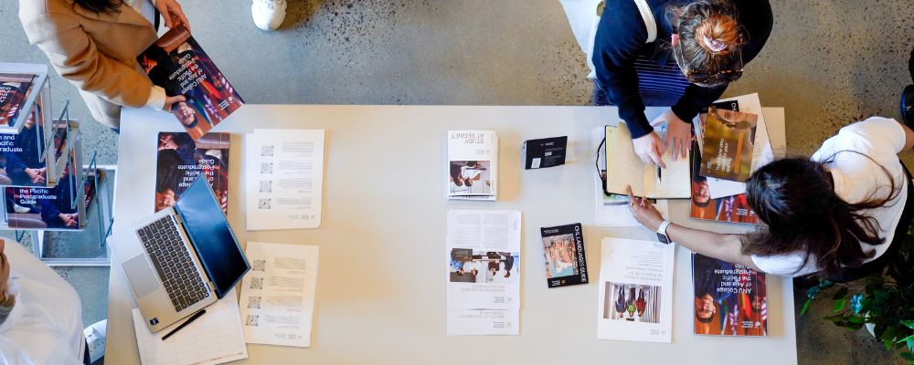 Shot from above of table with ANU Postgraduate Guides and prospective students interested.