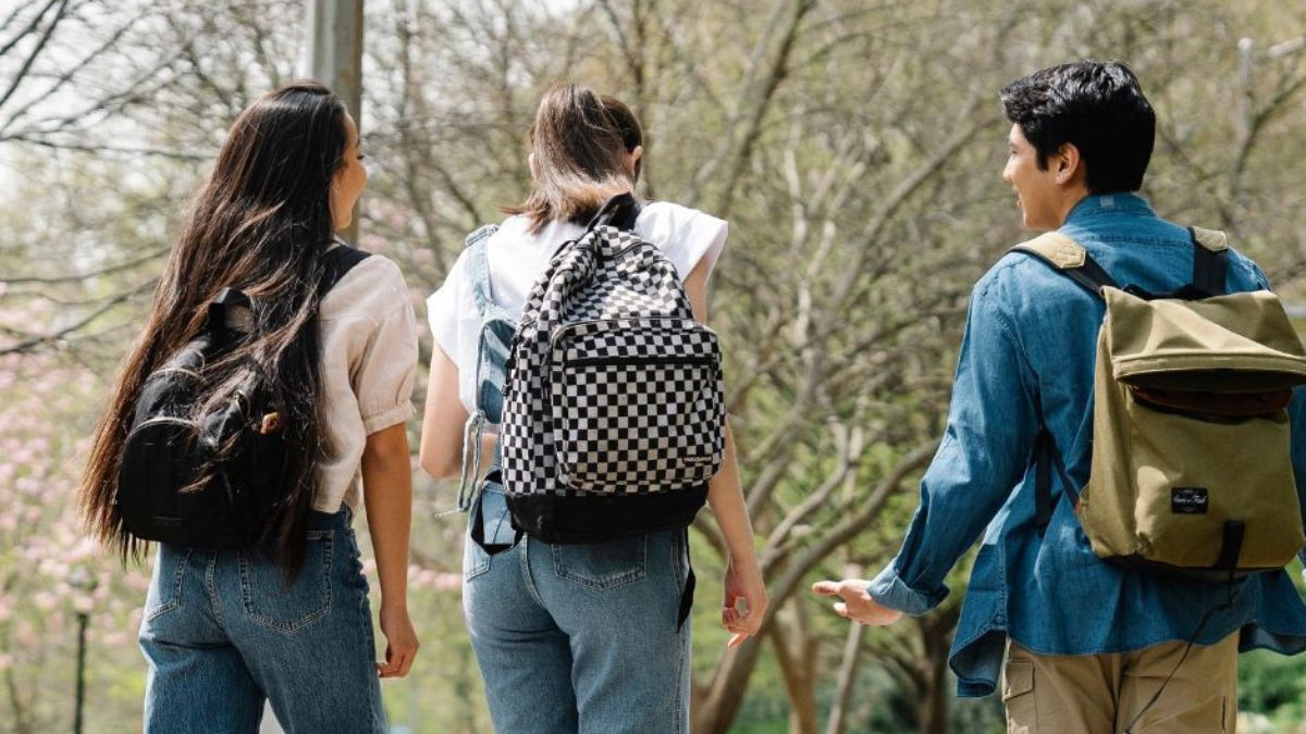 Three students walking from behind wearing backpacks on their backs. 