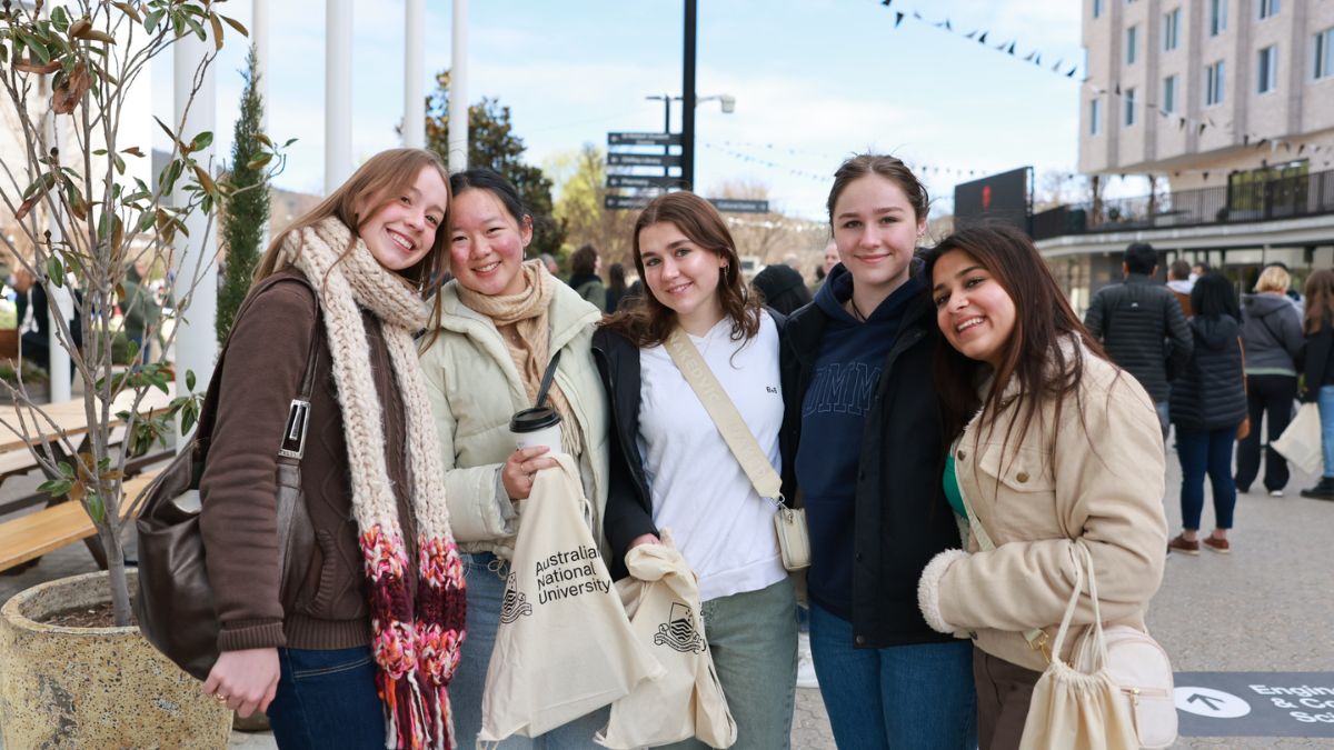 Five female ANU students smile at the camera as they stand on University Avenue. 