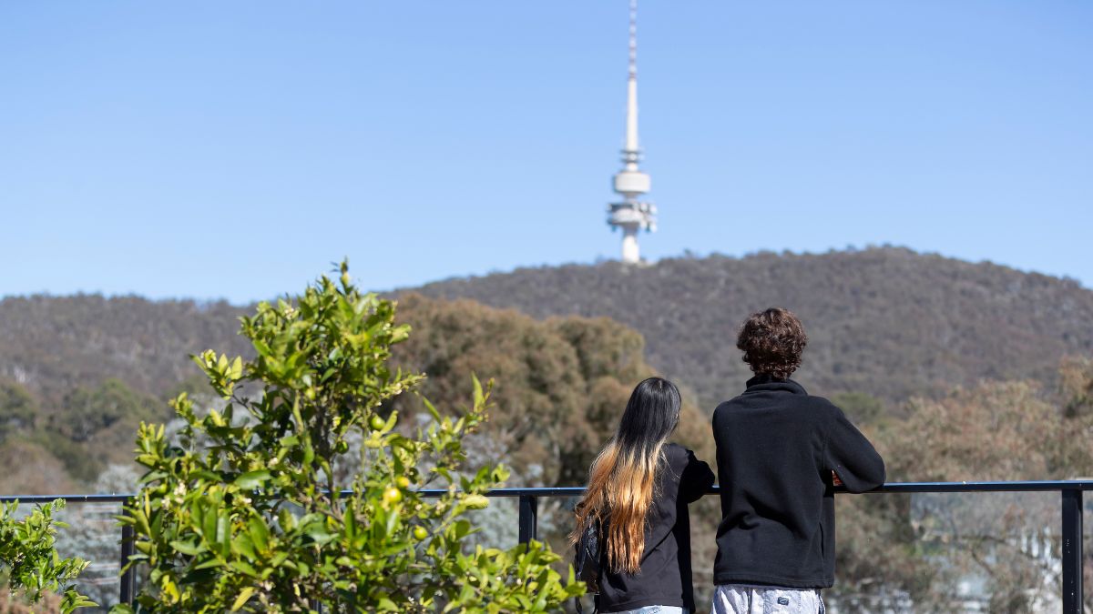 Two ANU students standing on a rooftop of student accommodation on campus looking towards Telstra Tower in Canberra.