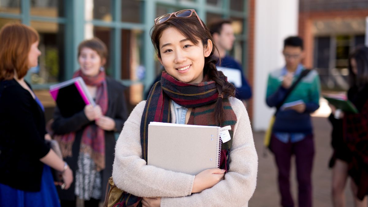 Female ANU student smiling at the camera holding study books.