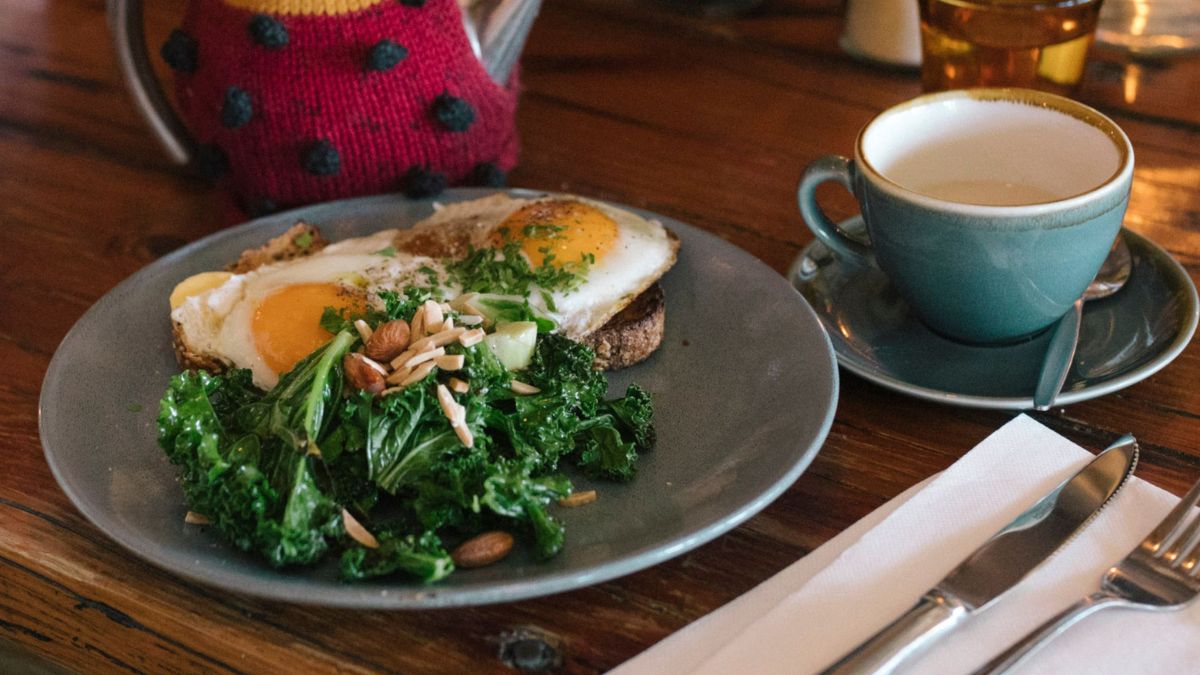 A picture of fried eggs and kale on sourdough toast with coffee on the side.