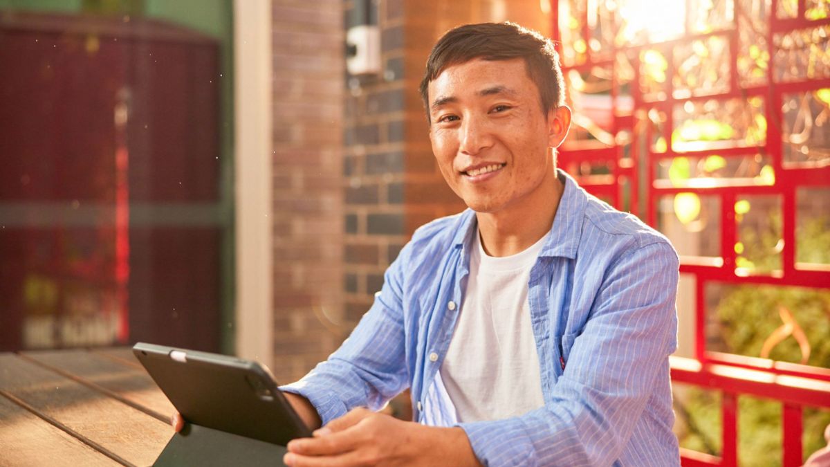 A male ANU student sits with a tablet in front of him on an outdoor table.
