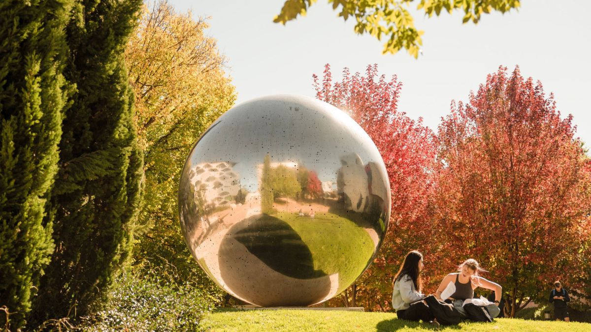Two students sit studying next to the Una Ball public art piece on campus at the Australian National University in Canberra
