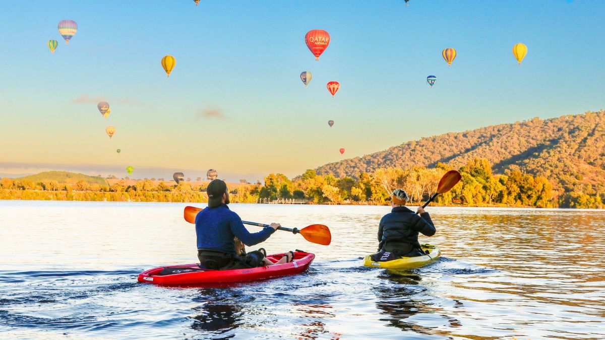 Two kayakers on Lake Burley Griffin in Canberra looking at the hot air balloons in the sky at sunrise.