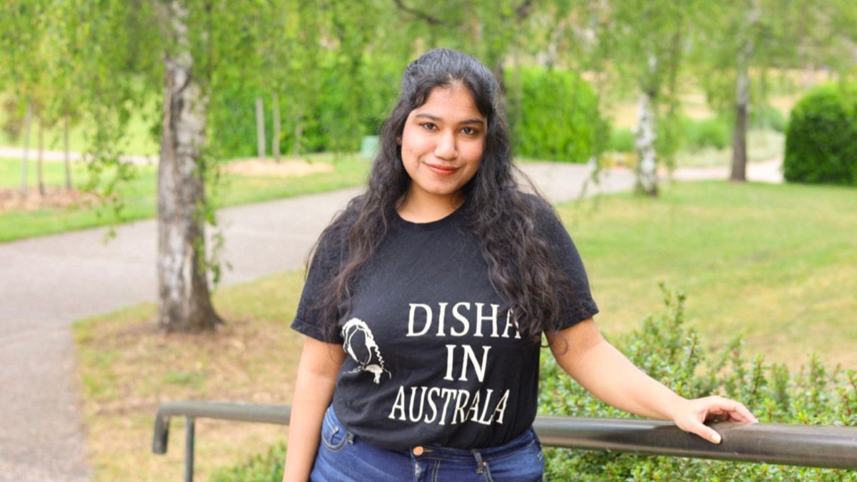 ANU student Disha stands against a rail on campus at the Australian National University.