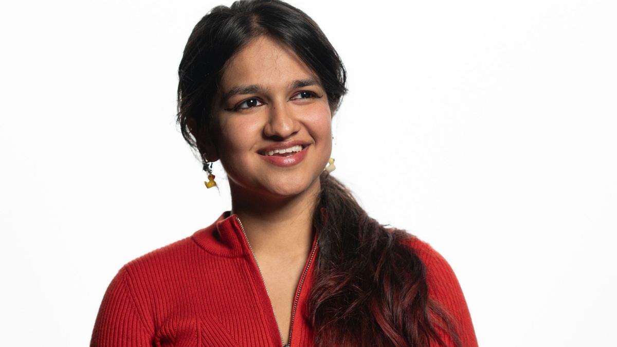 Tanya smiles at the camera in a photoshoot setting at the Australian National University in a red top.