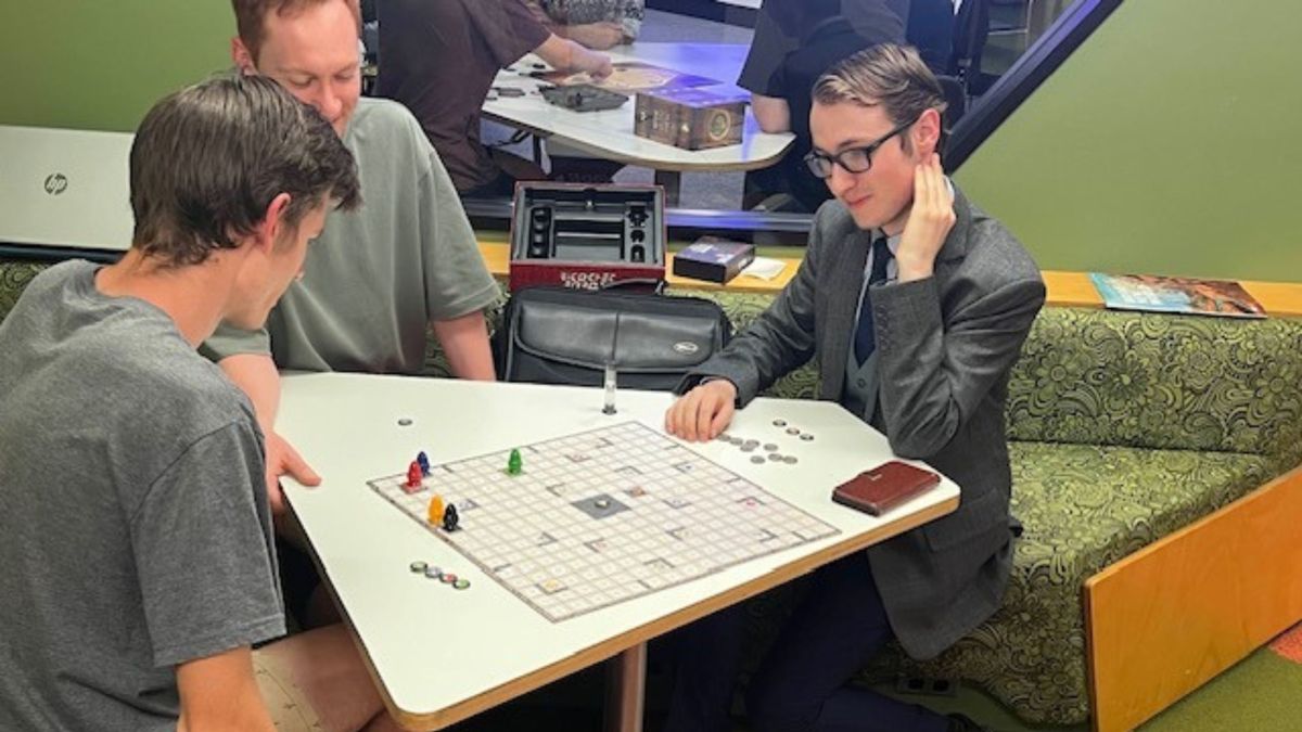 Three members of the ANU Board Games Society sit together around a game of Ricochet Robots.