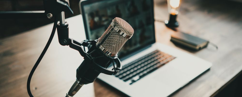 A laptop on a desk with podcast software installed including a podcast microphone.