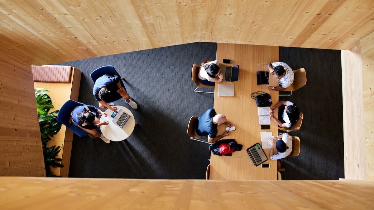 Overhead view of students seated at tables in a timber-lined study space, using laptops and notebooks in a collaborative learning environment.