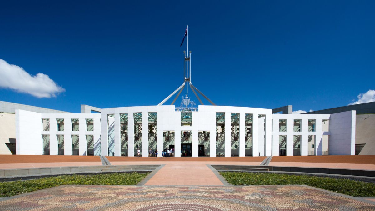 The exterior of Parliament House in Canberra taken from a front angle with a bright sunny day and blue sky behind the architecture
